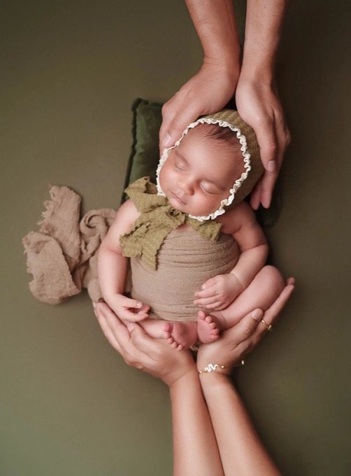 Vertical newborn baby photo at home with parents hands holding baby safely